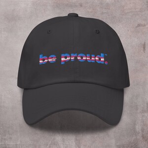 May include: Black baseball cap with the text "be proud." embroidered in blue, pink, and white stripes.