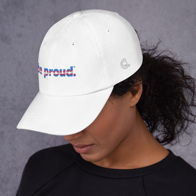 May include: White baseball cap with the text "Be proud." in blue, red, and white lettering. The text is in a stylized font with a thin blue line above and below the text.