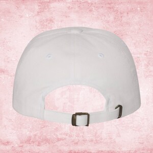 May include: White baseball cap with a brown adjustable buckle closure. The cap is made of a soft, cotton fabric.