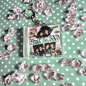 Puede incluir: Un llavero de plástico transparente con una tarjeta de foto insertada que presenta un collage de fotos de un grupo de K-pop. La tarjeta tiene un fondo rosa con acentos verdes y el texto "Want So Bad" en negro. El texto "Lee Know & Han" también es visible en la esquina superior derecha.