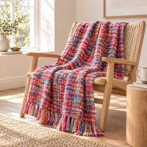 May include: A woven throw blanket featuring a vibrant multicolored pattern of red, blue, yellow, and purple threads. The rectangular textile has a textured, chunky knit appearance and is finished with long, multicolored fringe along the bottom edge.