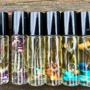 Puede incluir: Seis pequeñas botellas de vidrio con tapas de rodillo negras llenas de un líquido transparente y varias flores secas y cristales.