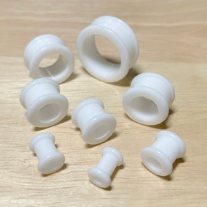 May include: Set of eight white acrylic ear gauges in various sizes. The gauges are smooth and have a simple design.