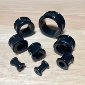 May include: A set of black acrylic ear gauges in various sizes. The gauges are smooth and have a shiny finish.