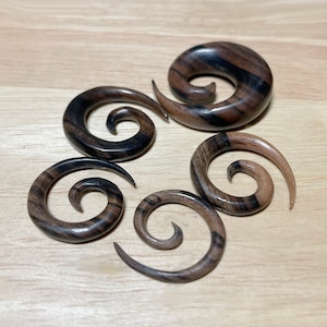 May include: Five wooden spiral ear gauges in various sizes. The gauges are made of dark brown wood with black streaks.