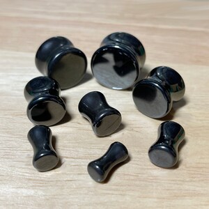 May include: A set of eight black hematite ear gauges in various sizes. The gauges are smooth and polished, with a slightly rounded edge.