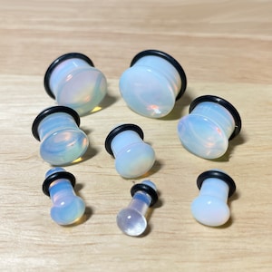 May include: Set of eight opalite ear gauges in various sizes. The gauges are made of clear opalite with a black rubber o-ring.