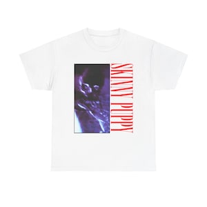 May include: White t-shirt featuring a rectangular graphic with a blurred, purple image and the text "SKINNY PUPPY" in red, vertically aligned on the right side. The shirt is a classic crew neck style.
