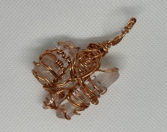 May include: A handcrafted pendant featuring clear quartz crystals wrapped in copper wire. The wire is intricately woven around the crystals, creating a unique design. The pendant has a loop for a chain.