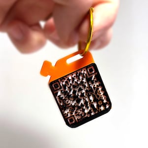 Op de afbeelding: Oranje sleutelhanger met een zwart-witte QR-code. De sleutelhanger heeft een gouden ring.
