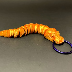 May include: Orange alligator keychain with a segmented body and a purple metal ring.