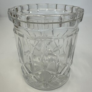 May include: A clear, faceted glass tumbler with a geometric design. The glass has a thick, textured rim and a diamond-shaped pattern on the body. The tumbler is empty and sits on a white surface.