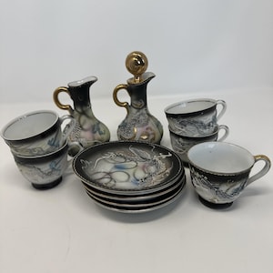 May include: A vintage Japanese porcelain tea set with a black and white dragon design. The set includes cups, saucers, and two decorative pitchers with gold accents. The set is a complete tea service.