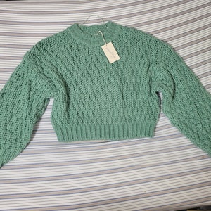 May include: A green chunky knit sweater with a round neckline. The sweater is cropped and has long sleeves.