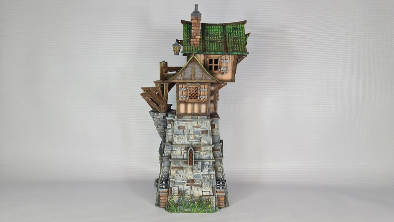 May include: A miniature model of a stone tower with a wooden house built on top. The house has a green roof and a small window. The tower has a stone wall with a small window and a door. The model is painted in realistic colors.