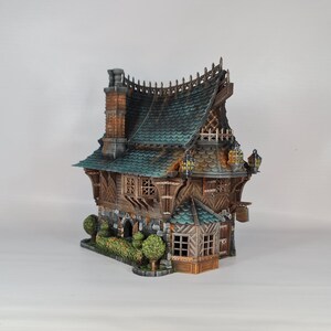 May include: A detailed miniature house with a teal roof, brick chimney, and wooden siding. The model features intricate architectural details, including small windows, decorative trim, and a small garden with bushes. The overall color palette is earthy with hints of teal and brown.