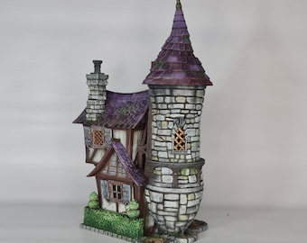 May include: A miniature stone tower with a pointed roof and a smaller building attached to the side. The tower has a window with a lattice design and the roof is a dark purple color. The building has a brown door and windows with shutters.