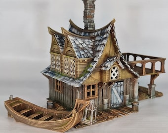 Può includere: Una casa in legno in miniatura con un tetto di tegole grigie, un camino e una piccola barca attraccata davanti. La casa ha una porta e finestre in legno e un piccolo balcone sul lato. La casa è dipinta in tonalità di marrone, grigio e bianco.