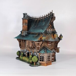 May include: A detailed miniature fantasy house with a green tiled roof, wooden walls, and stone foundation. The model features a chimney, decorative trim, and small trees. Lanterns hang from the eaves, adding to the whimsical design.