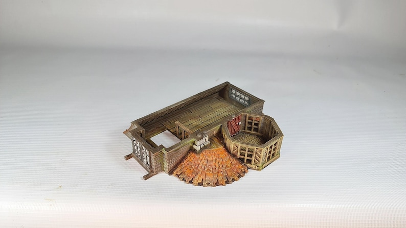 A painted miniature of a fantasy building's interior, showing wooden floors and a partial roof structure, with no walls.