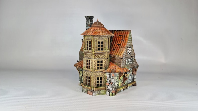 A painted miniature of a two-story fantasy building with a red-orange tiled roof, stone foundation, and wooden walls, viewed from the back-right, with "VENE 1553" carved into the back.