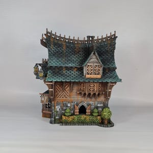 May include: A detailed miniature fantasy house with a green tiled roof, wooden walls, and stone accents. The house features decorative lanterns, a small arched doorway, and a detailed facade. The overall design evokes a whimsical, storybook aesthetic.