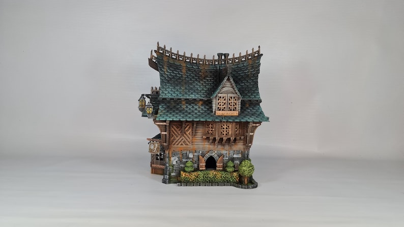 May include: A detailed miniature fantasy house with a green tiled roof, wooden walls, and stone accents. The house features decorative lanterns, a small arched doorway, and a detailed facade. The overall design evokes a whimsical, storybook aesthetic.