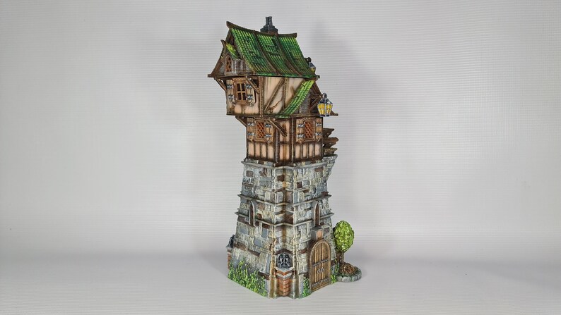 May include: A miniature model of a crooked, multi-level building with a green roof, stone walls, and wooden accents. The building has a small door and windows, and a small tree is growing next to it.