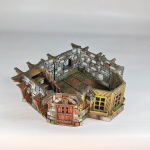 A painted miniature of a fantasy building's interior, showing stone walls, wooden floors, and a staircase, with no roof.
