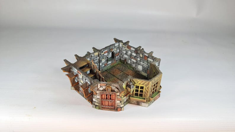 A painted miniature of a fantasy building's interior, showing stone walls, wooden floors, and a staircase, with no roof.