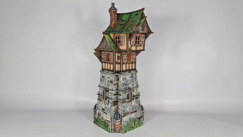 May include: A miniature model of a stone tower with a wooden house perched on top. The house has a green roof and brown wooden walls with windows. The tower is made of gray stone with a brown brick base.