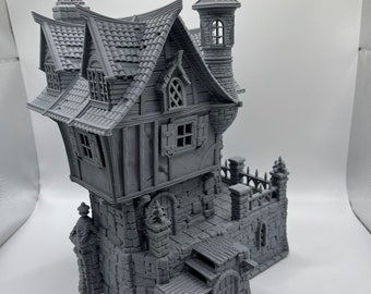 May include: A gray 3D printed model of a stone building with a pointed roof, a tower, and a set of stairs leading to a door. The building has several windows and a chimney.