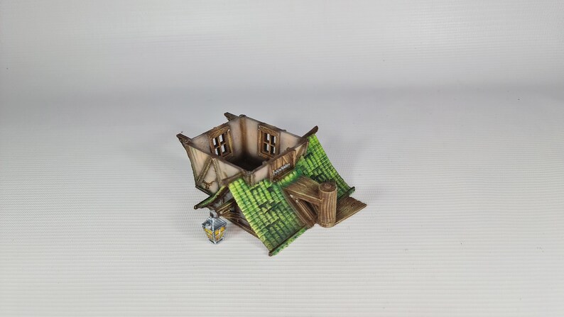May include: A miniature wooden house with a green roof and two windows. The house has a small porch and a lantern hanging from the side.