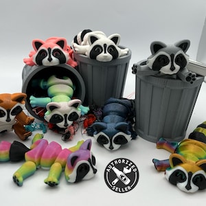 Pode incluir: Uma coleção de figuras de guaxinins coloridos, algumas em latas de lixo, outras deitadas sobre uma superfície branca. Os guaxinins são feitos de plástico impresso em 3D e têm uma variedade de cores, incluindo rosa, branco, marrom, azul e arco-íris.