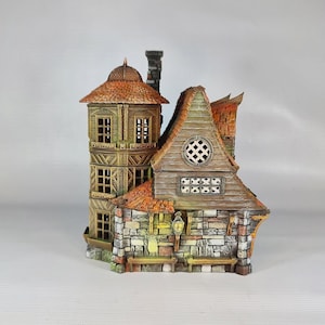 A painted miniature of a two-story fantasy building with a red-orange tiled roof, stone foundation, and wooden walls, viewed from the back, with a round window and a hanging lantern.