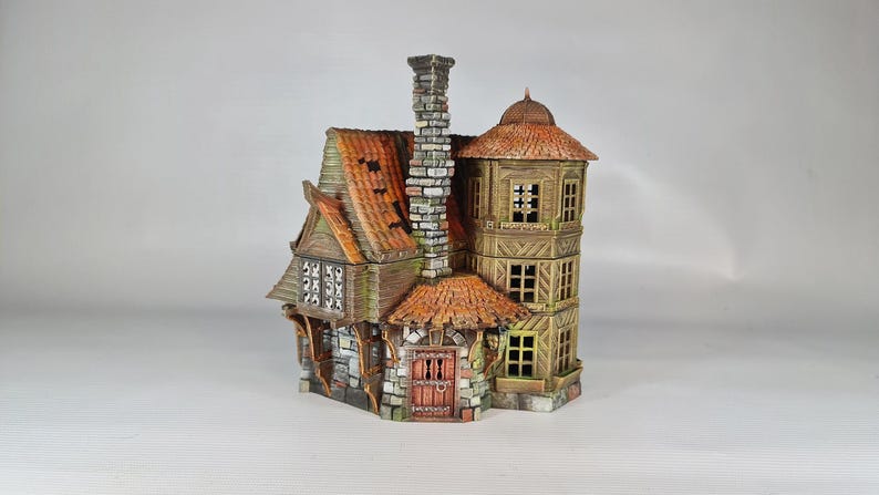 A painted miniature of a two-story fantasy building with a red-orange tiled roof, stone foundation, and wooden walls, viewed from the front-left, showing a tall chimney.