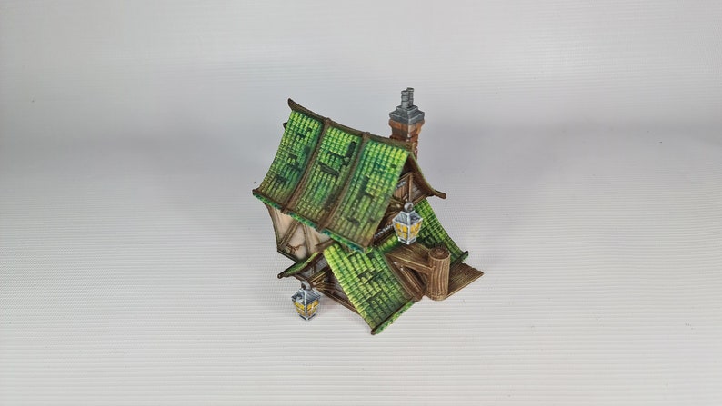 May include: A miniature wooden house with a green tiled roof and a chimney. The house has two windows and a door, and there are lanterns hanging from the eaves.