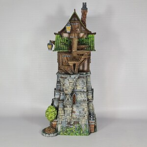 May include: A miniature wooden tower with a green roof and stone base. The tower has a small window and a chimney. The tower is surrounded by green foliage.