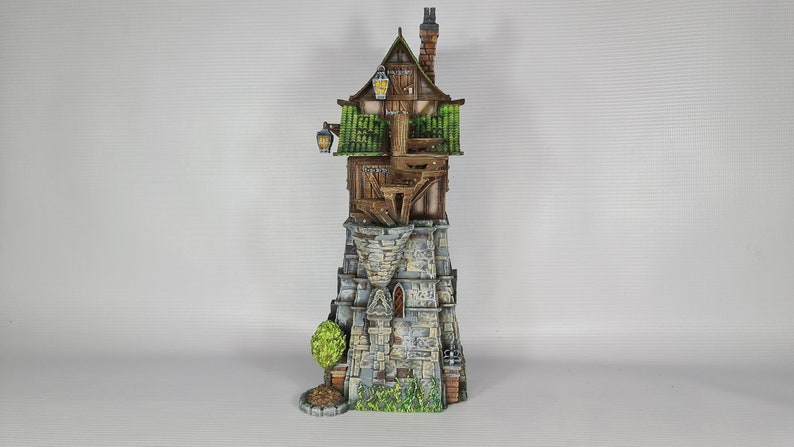 May include: A miniature wooden tower with a green roof and stone base. The tower has a small window and a chimney. The tower is surrounded by green foliage.