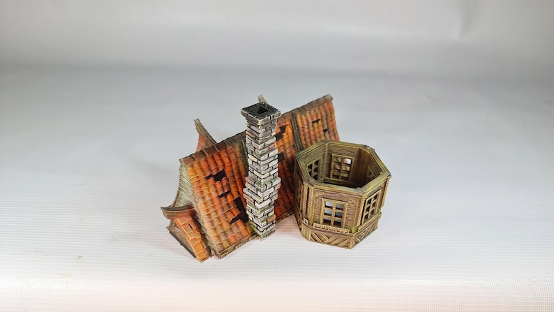 A painted miniature of a fantasy building's roof section with a chimney, and a separate multi-level turret, both with red-orange tiles.