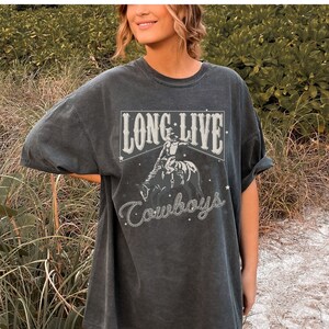 May include: A dark gray oversized t-shirt with a vintage-style graphic print of a cowboy riding a horse. The graphic includes the text "Long Live Cowboys" with stars and a rope design.