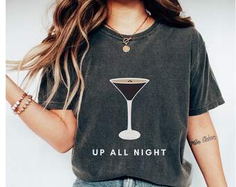May include: A dark gray t-shirt with a graphic of a martini glass filled with coffee and the text "Up All Night".