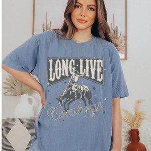 May include: A blue oversized t-shirt with a vintage graphic design featuring a cowboy riding a horse. The graphic says "Long Live Cowboys" with stars and a rope design.