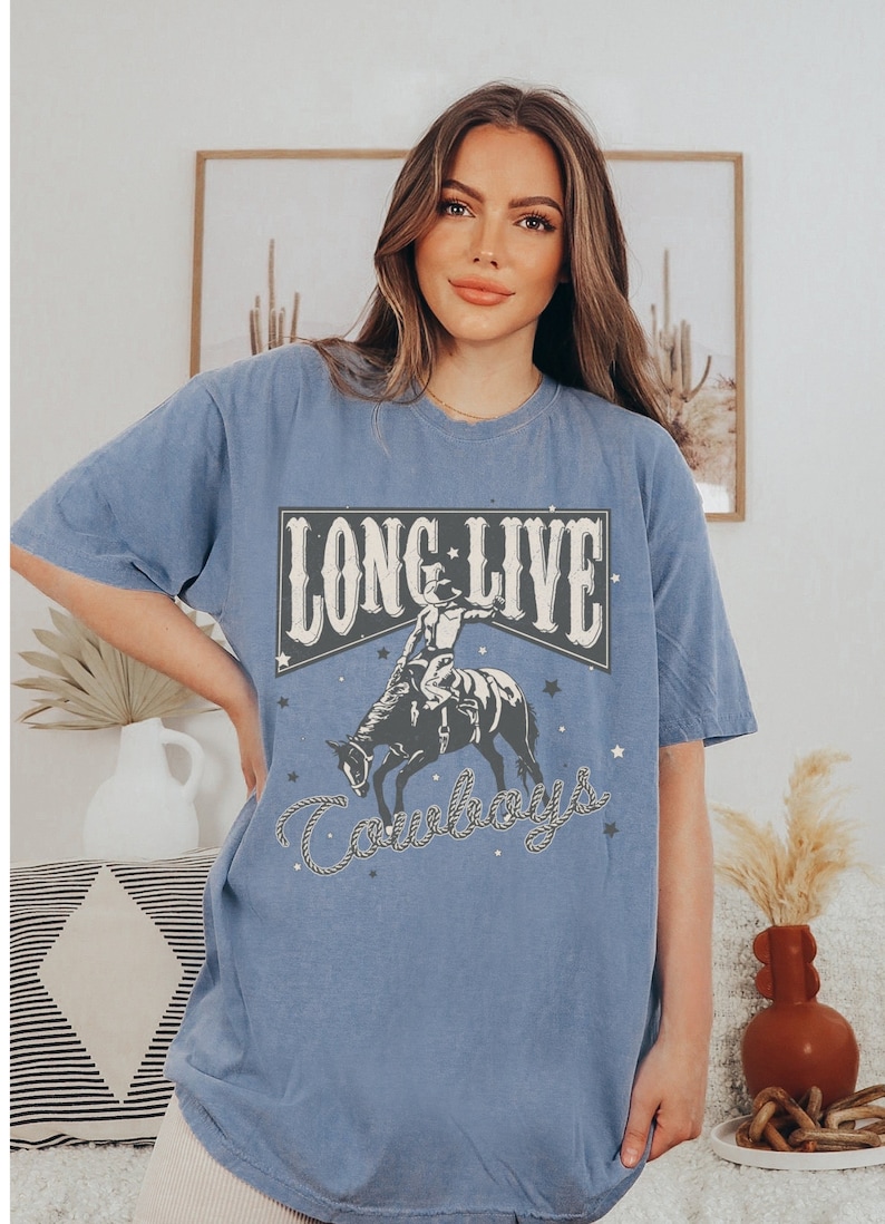 May include: A blue oversized t-shirt with a vintage graphic design featuring a cowboy riding a horse. The graphic says "Long Live Cowboys" with stars and a rope design.