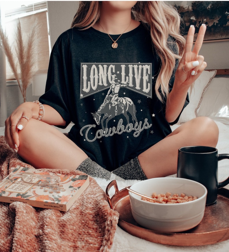 May include: A black t-shirt with a vintage-style graphic of a cowboy riding a horse. The graphic includes the text "Long Live Cowboys" in a white banner.