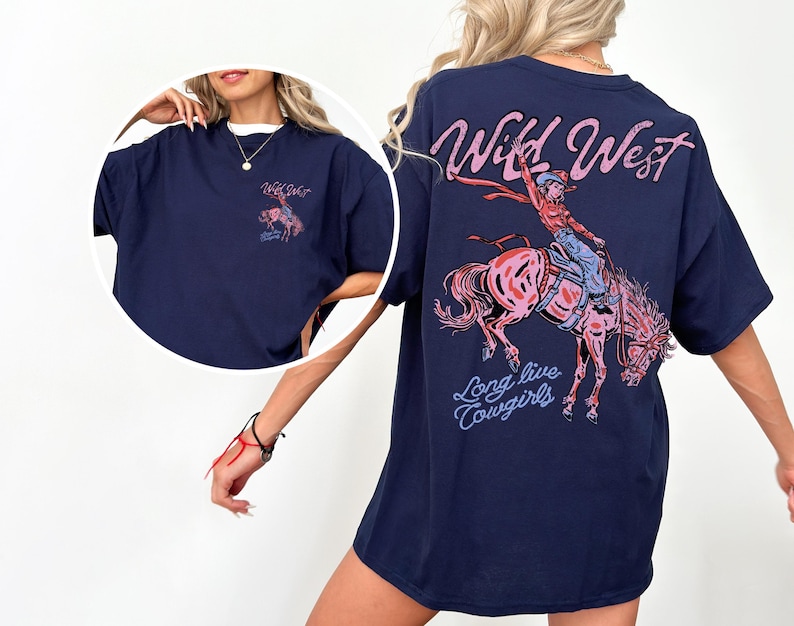 Puede incluir: Camiseta azul marino con un dise&ntilde;o de una vaquera montando un caballo salvaje, con las palabras "Wild West" y "Long live Cowgirls" en rosa y azul. La camiseta tiene un corte holgado.
