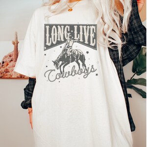 May include: White oversized t-shirt with a graphic print of a cowboy riding a bucking horse. The graphic includes the text "Long Live Cowboys" with stars and a rope design.