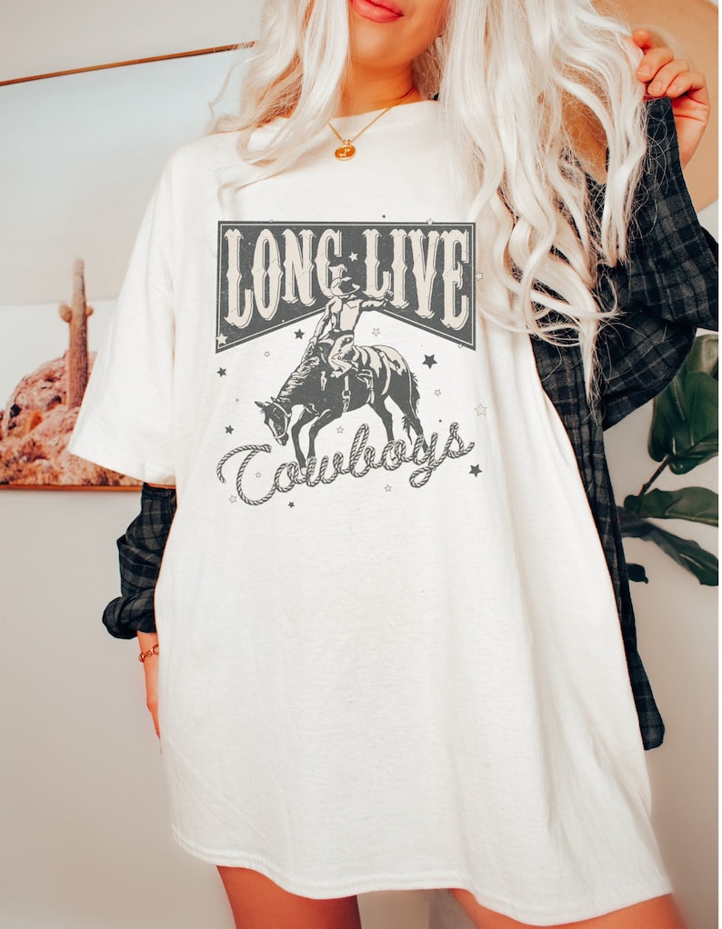 May include: White oversized t-shirt with a graphic print of a cowboy riding a bucking horse. The graphic includes the text "Long Live Cowboys" with stars and a rope design.