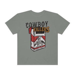 Peut inclure: Un t-shirt gris avec un imprim&eacute; vintage d'un paquet de cigarettes avec le texte "COWBOY KILLERS" imprim&eacute; dessus.