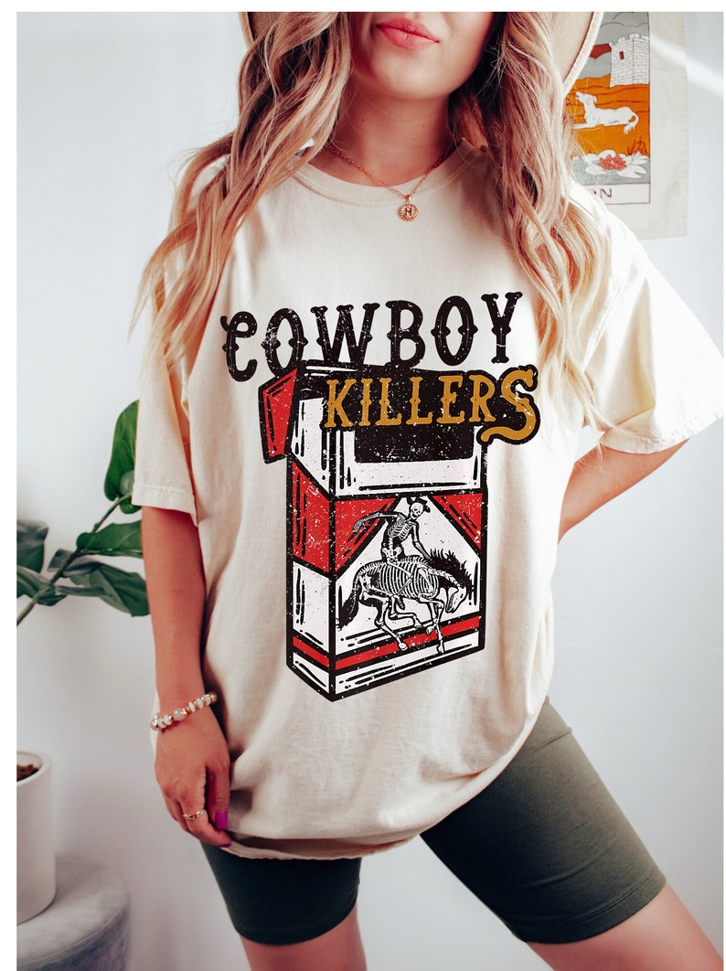 Peut inclure: Un t-shirt cr&egrave;me avec un graphique vintage d'un paquet de cigarettes qui dit "Cowboy Killers". Le graphique repr&eacute;sente un squelette &agrave; cheval.